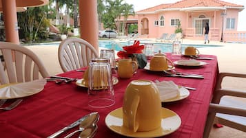 A dining table set with yellow plates, clear glassware, and a red tablecloth.