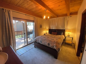 Un dormitorio con una cama grande, techo de madera, puerta corrediza de vidrio a una terraza y dos lámparas de noche.