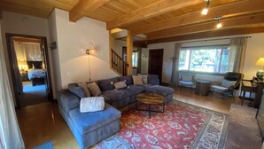 A spacious living room with a large sectional sofa, a coffee table, and a patterned rug. There is a staircase leading to another level, and a window with curtains. - Private neighborhood beach, gated community. 3 miles from casinos -8ppl (Zephyr Cove)