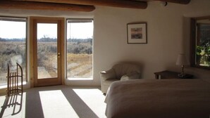 Un dormitorio con una cama grande, un sillón mecedora, una mesita de noche con una lámpara y un cuadro enmarcado en la pared.