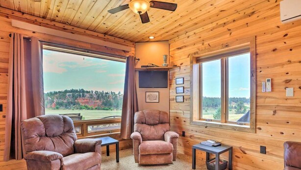 Una habitación acogedora con paredes de madera, dos sillones de cuero, una mesita y un ventilador de techo.