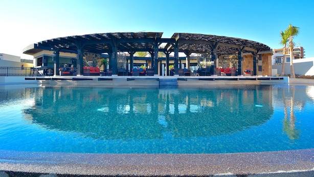 Un espace piscine doté d’un coin salon abrité et d’un bâtiment en arrière-plan.