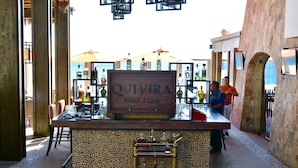 Un espace bar avec une enseigne indiquant « QUIVIRA GOLF CLUB », un présentoir de bouteilles d’alcool et un coin salon avec des chaises et des tables.