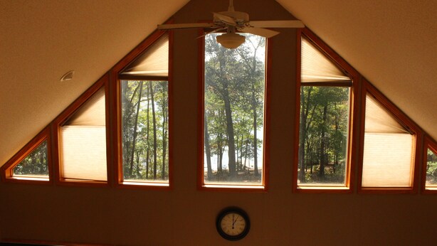 A room with a sloped ceiling, a ceiling fan, and a clock on the wall. There are three windows with blinds, and a view of trees outside. - Heron Landing:  Escape to Lake Mayo.
Private cove, where nature abounds! 



 (Roxboro)