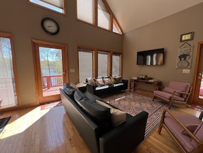A spacious living room with a large black leather sofa, a wooden coffee table, and a television mounted on the wall. There are large windows with blinds, a red deck, and a view of a lake. - Heron Landing: Escape to Lake Mayo.
Private cove, where nature abounds!
(Roxboro)