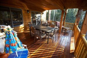 A wooden deck with a table and chairs, large windows, and a view of trees.