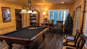 Una habitación acogedora con mesa de billar, estanterías de madera, un árbol de Navidad y asientos cómodos.