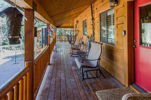 A wooden porch with a red door, a bench, and a hanging light fixture.
