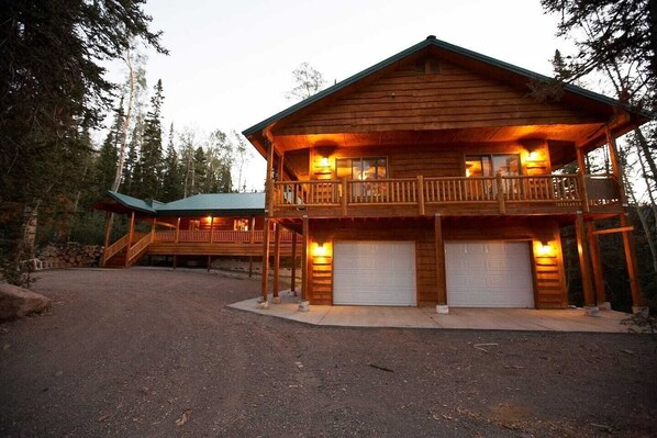 A two-story log cabin with a balcony, a covered porch, and two garage doors.