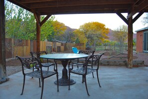 An outdoor patio with a round table and four chairs, surrounded by a wooden fence and trees with autumn foliage.