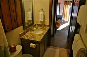 A bathroom with a marble sink, wooden cabinets, a toilet, and a mirror.