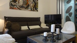 A modern living room with a dark sofa, a flat-screen TV, a glass coffee table with candles, and a painting on the wall. - Luxury stay with champagne in an Artist's Atelier In The 5th (Paris)