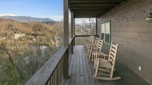 A wooden deck with rocking chairs overlooking a mountainous landscape. - GREAT view DOWNTOWN Gatlinburg with views,community pool, hot tub and fireplace (Gatlinburg)