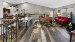 A spacious living area with a wooden-floored floor, a red sofa, a foosball table, and a dining table. - GREAT view DOWNTOWN Gatlinburg with views,community pool, hot tub and fireplace (Gatlinburg)