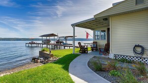 Ein Anwesen am Seeufer mit überdachter Terrasse, Sitzgelegenheiten im Freien und einer Anlegestelle für Boote.