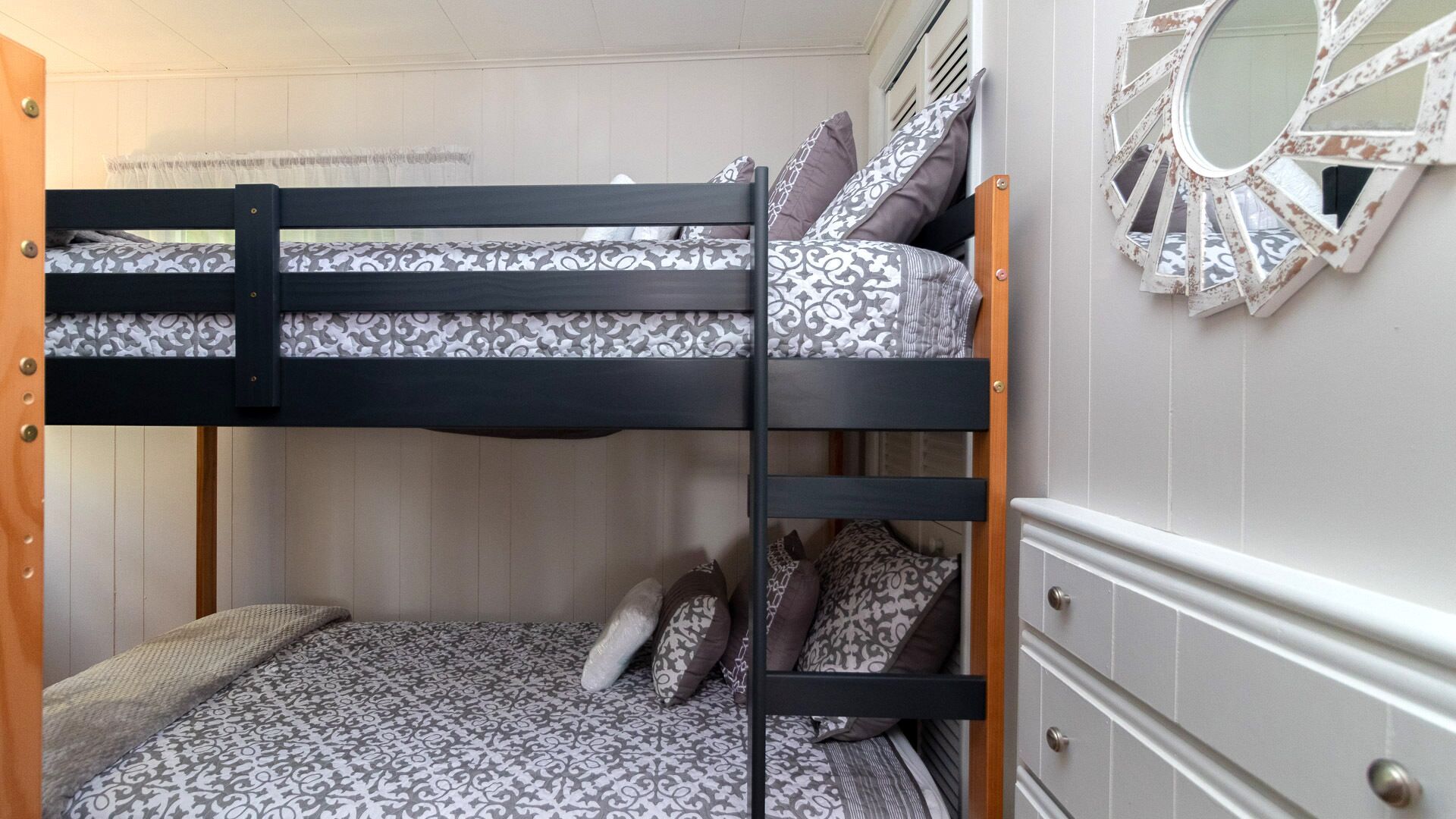 Uma cama beliche com roupa de cama estampada, uma escada de madeira e uma cômoda com gavetas.