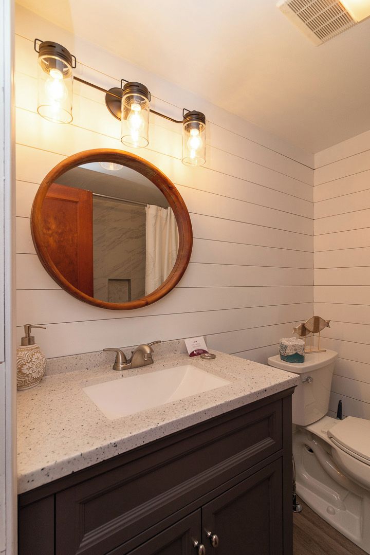 A bathroom with a round mirror, a white sink, a dark wooden vanity, and a toilet.
