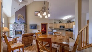 A spacious living room with a fireplace, wooden furniture, and a kitchen in the background.