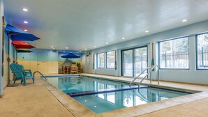 An indoor swimming pool with clear blue water, surrounded by windows and a concrete floor.