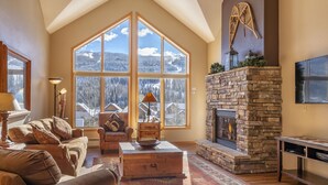 A cozy living room with a fireplace, large windows, and a stone accent wall.