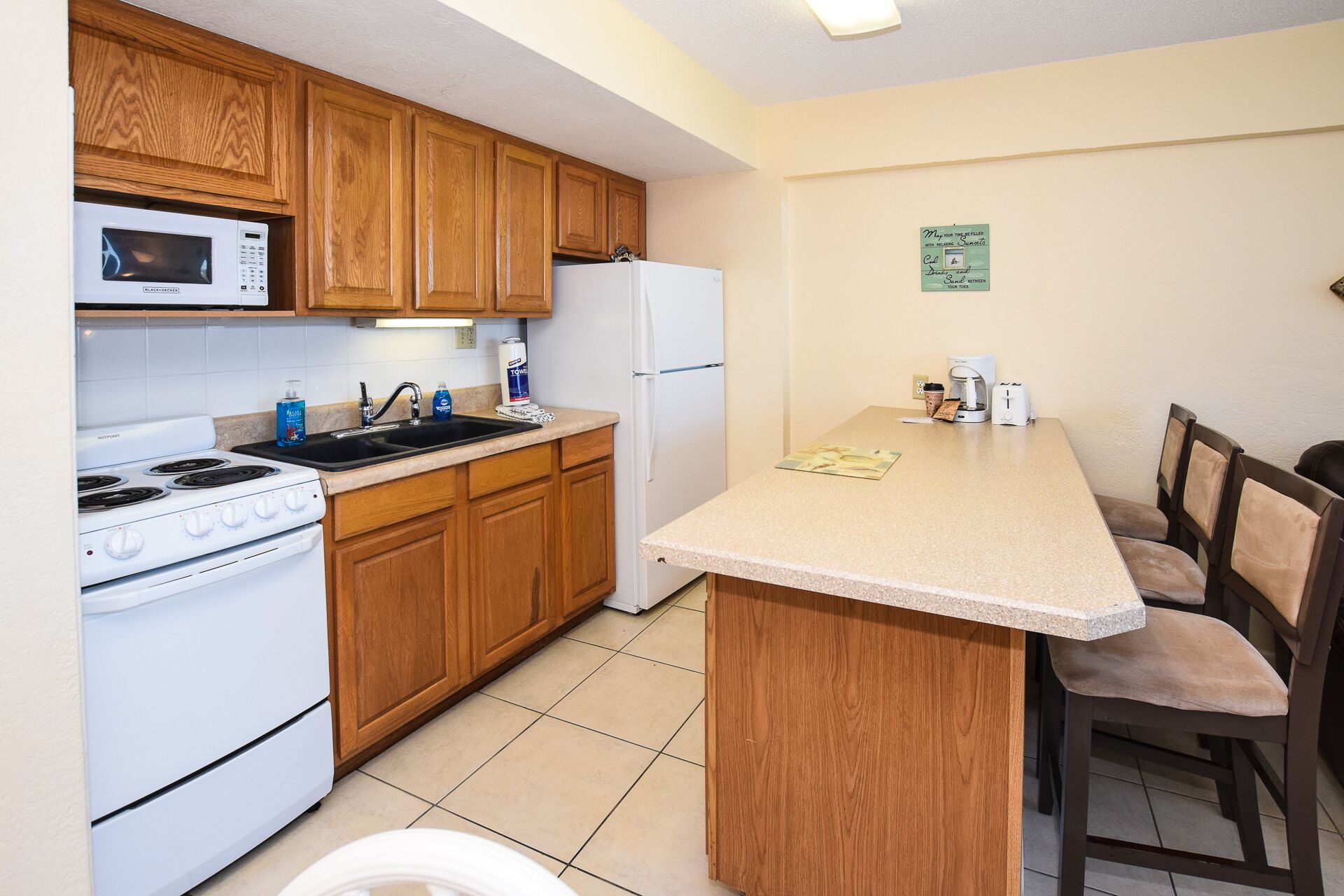 Cocina compacta con muebles de madera, microondas, estufa, refrigerador y un pequeño comedor con mesa y sillas.