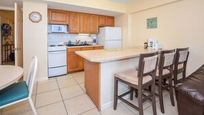 A compact kitchen with wooden cabinets, a microwave, a stove, and a refrigerator. There is a small dining area with a table and chairs.