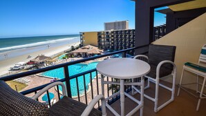 A balcony with a pool, lounge chairs, and a view of the beach and ocean.