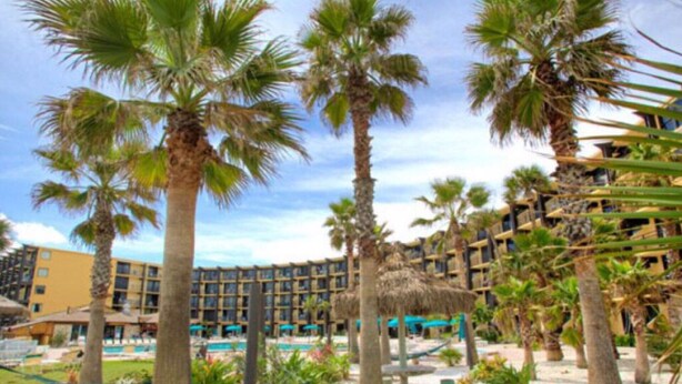 A resort with palm trees, a pool, and a building with multiple balconies.