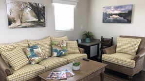 A living room with a sofa, armchair, coffee table, and two wall-mounted paintings.
