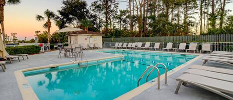 Una piscina con sillas de descanso y un edificio pequeño al fondo.