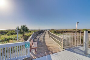 Une promenade en bois menant à une plage, avec un banc et un panneau indiquant les heures d’accès à la plage.