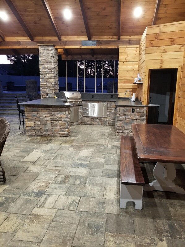 An outdoor kitchen with stone and wood accents, a grill, and a sink.