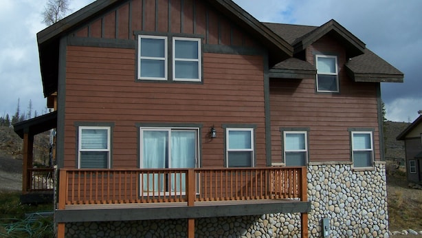 A two-story house with a stone foundation, a wooden deck, and multiple windows.