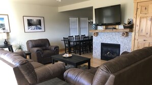 A living room with leather sofas, a coffee table, a fireplace, a TV, and a dining area with chairs and a table.