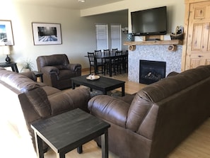 Una sala de estar con sofás de cuero, una mesa de centro, una chimenea, un televisor y un comedor con sillas y una mesa.