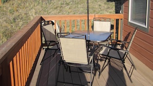 A deck with a table and chairs, an umbrella, and a view of a hilly landscape.