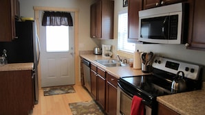A kitchen with wooden cabinets, a microwave, a stove, a sink, and a window with a curtain.