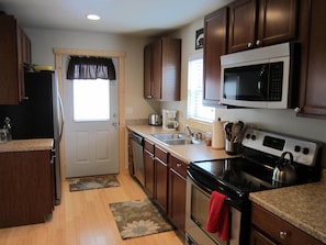 Una cocina con armarios de madera, microondas, estufa, lavabo y una ventana con cortina.