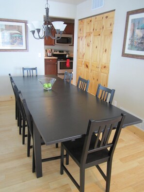 Comedor con una larga mesa, sillas, una araña, microondas y armarios de madera.