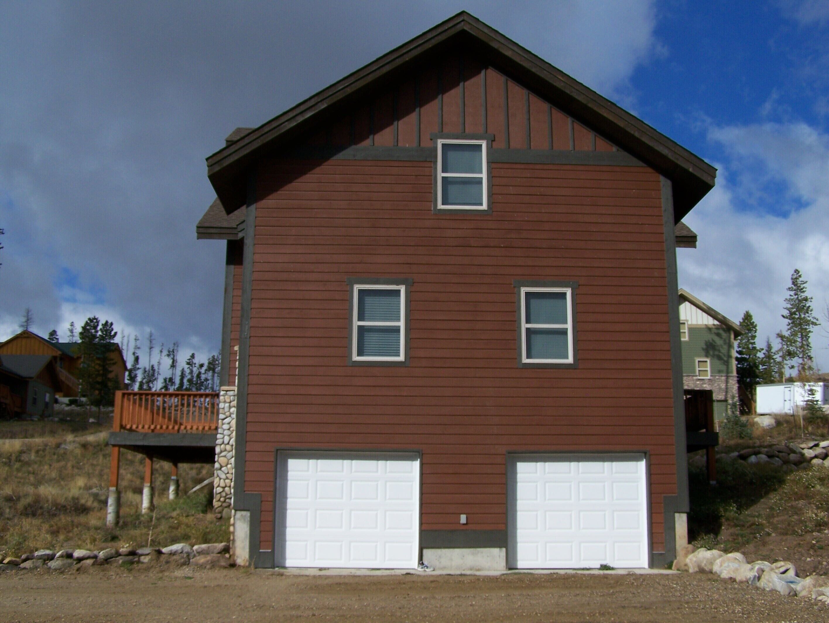 Une maison à deux étages, avec une façade marron, deux portes de garage et une petite fenêtre au deuxième étage.