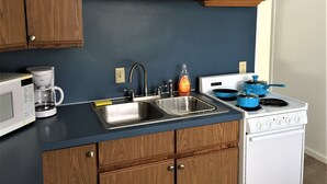 Een keuken met houten kastjes, een blauw aanrecht, een roestvrijstalen spoelbak, een koffiezetapparaat, een waterkoker en een fornuis.