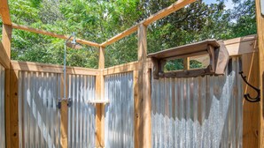 Una estructura de madera con un muro de metal corrugado, techo de madera y ducha de metal.