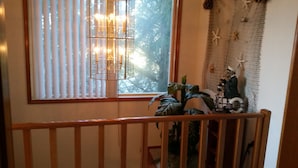 Quarto com grade de madeira, janela com persianas, luminária pendente e decoração de parede com uma figura e estrelas-do-mar.