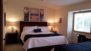 Quarto com uma cama grande, duas mesas de cabeceira com abajures, um criado-mudo e uma janela com persianas.
