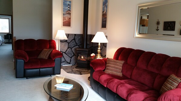 A cozy living room with two red sofas, a glass coffee table, a fireplace, and nautical-themed wall art.