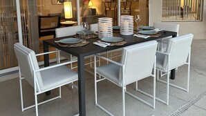 Een eethoek met een tafel voor meerdere personen, witte stoelen en een glazen scheiding.