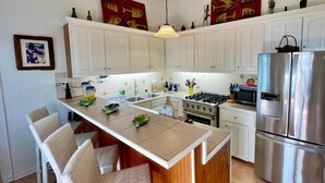 Una cocina moderna con armarios blancos, un refrigerador de acero inoxidable, una estufa a gas y una isla central con sillas.