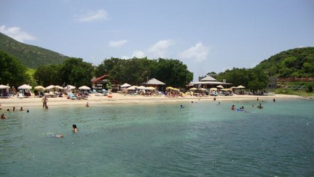 Una playa con agua cristalina, sombrillas y gente nadando.