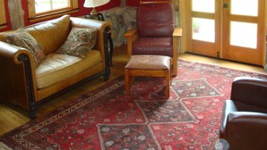 Une pièce chaleureuse avec un plafond en bois, un mur rouge, un tapis à motifs, un fauteuil en cuir, une table en bois et une fenêtre donnant sur un beau paysage.