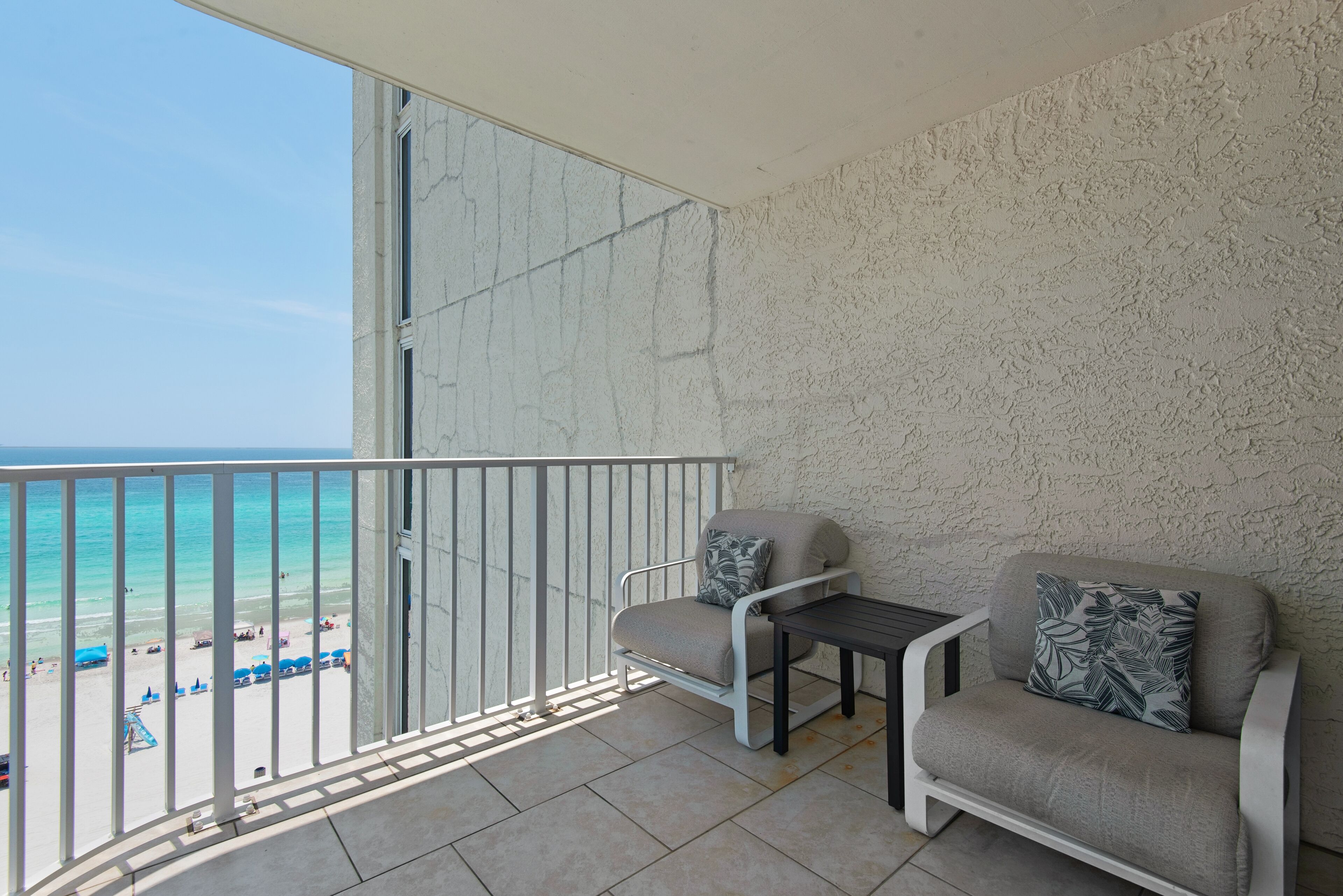 Un balcón con vista a la playa, un sofá, una mesita y una silla.